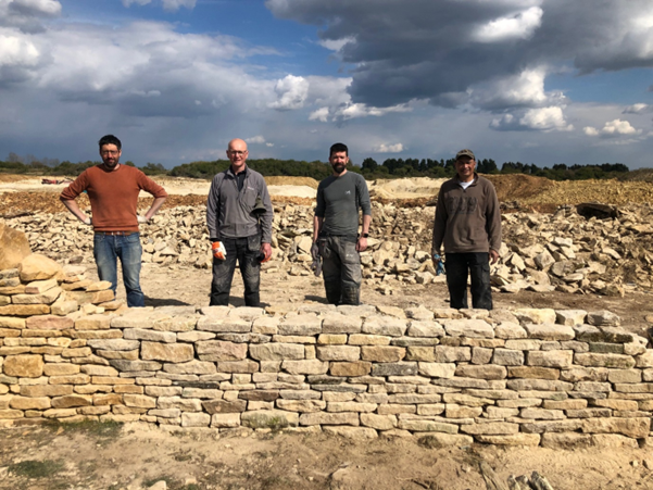 Finished dry stone wall built during a workshop, with workshop participants standing behind it